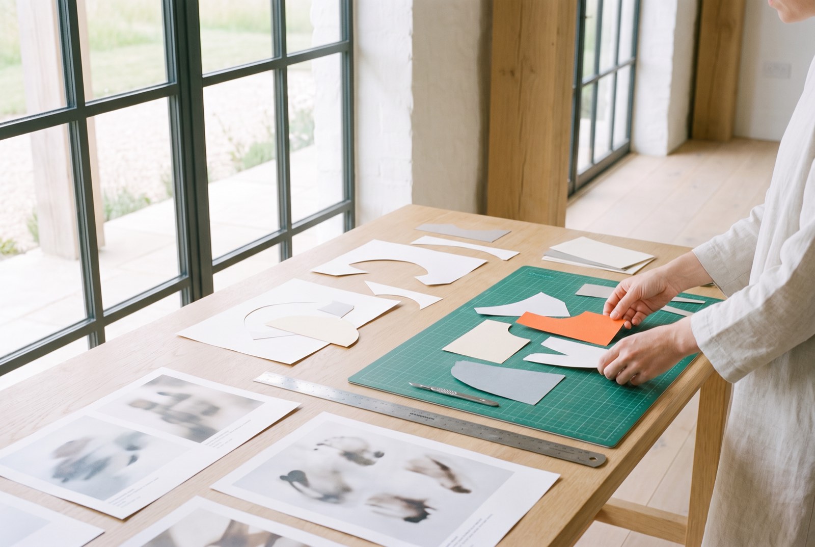 Hands arrange paper cut-outs and printed pages on a cutting mat.
